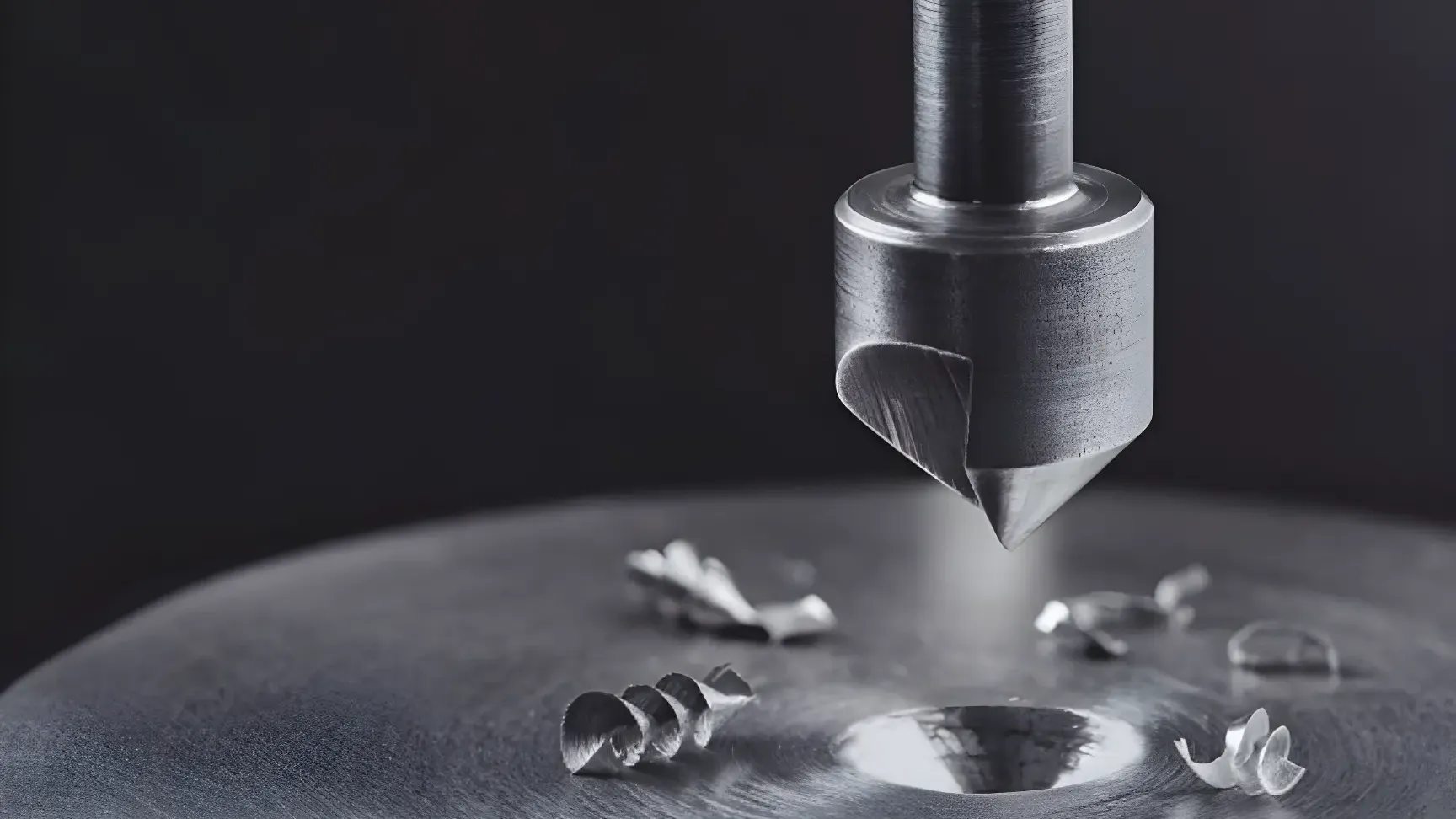 Countersink drill bit cutting a chamfered hole in a steel plate, with curled metal shavings scattered around