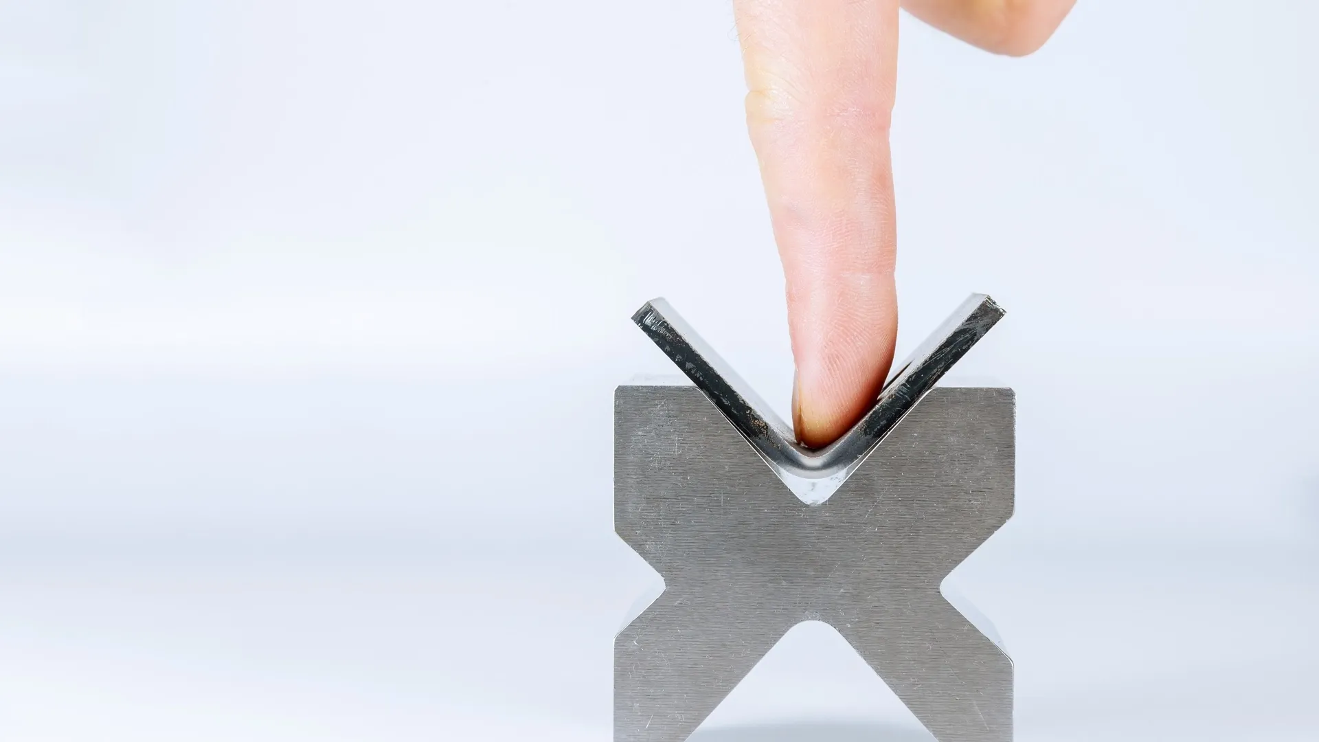 Close-up of a finger pressing a thin metal strip into a V-die by hand