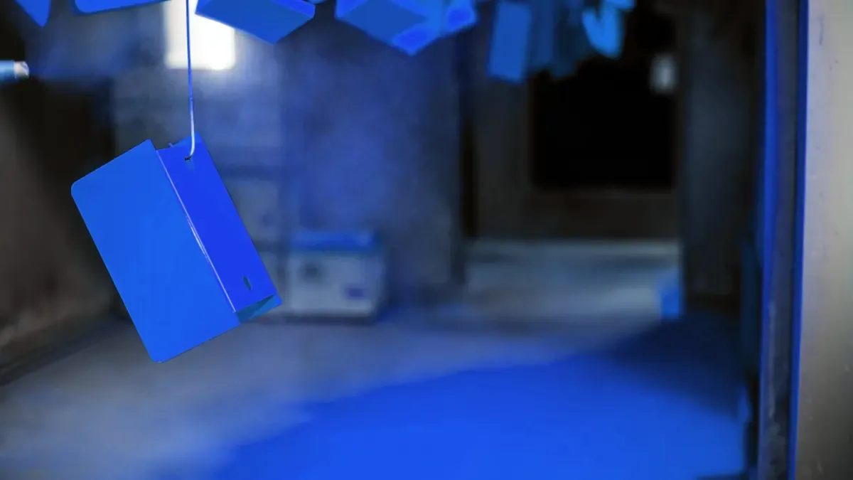 Blue powder-coated bracket hanging from a hook inside a powder coat booth