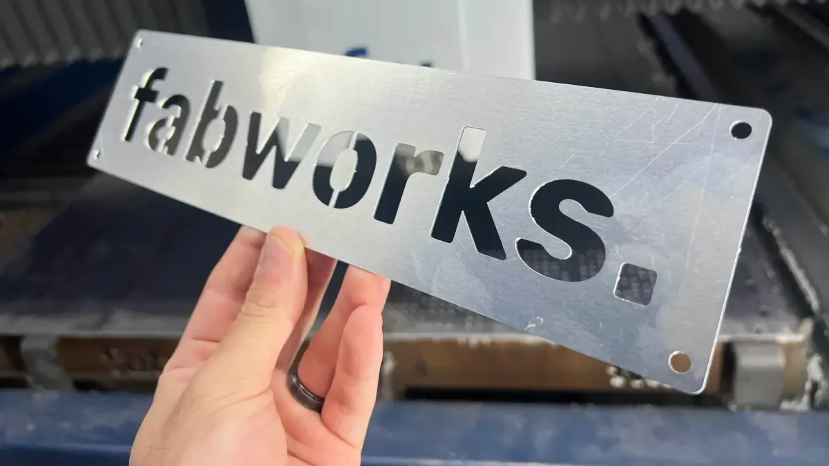 Laser-cut metal sign spelling "fabworks." held in front of the cutting machine