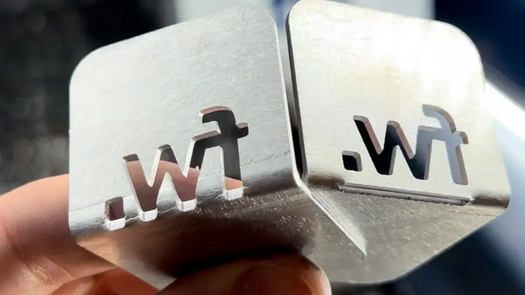 Two identical laser-cut metal tags with a small logo cutout, held side by side for comparison