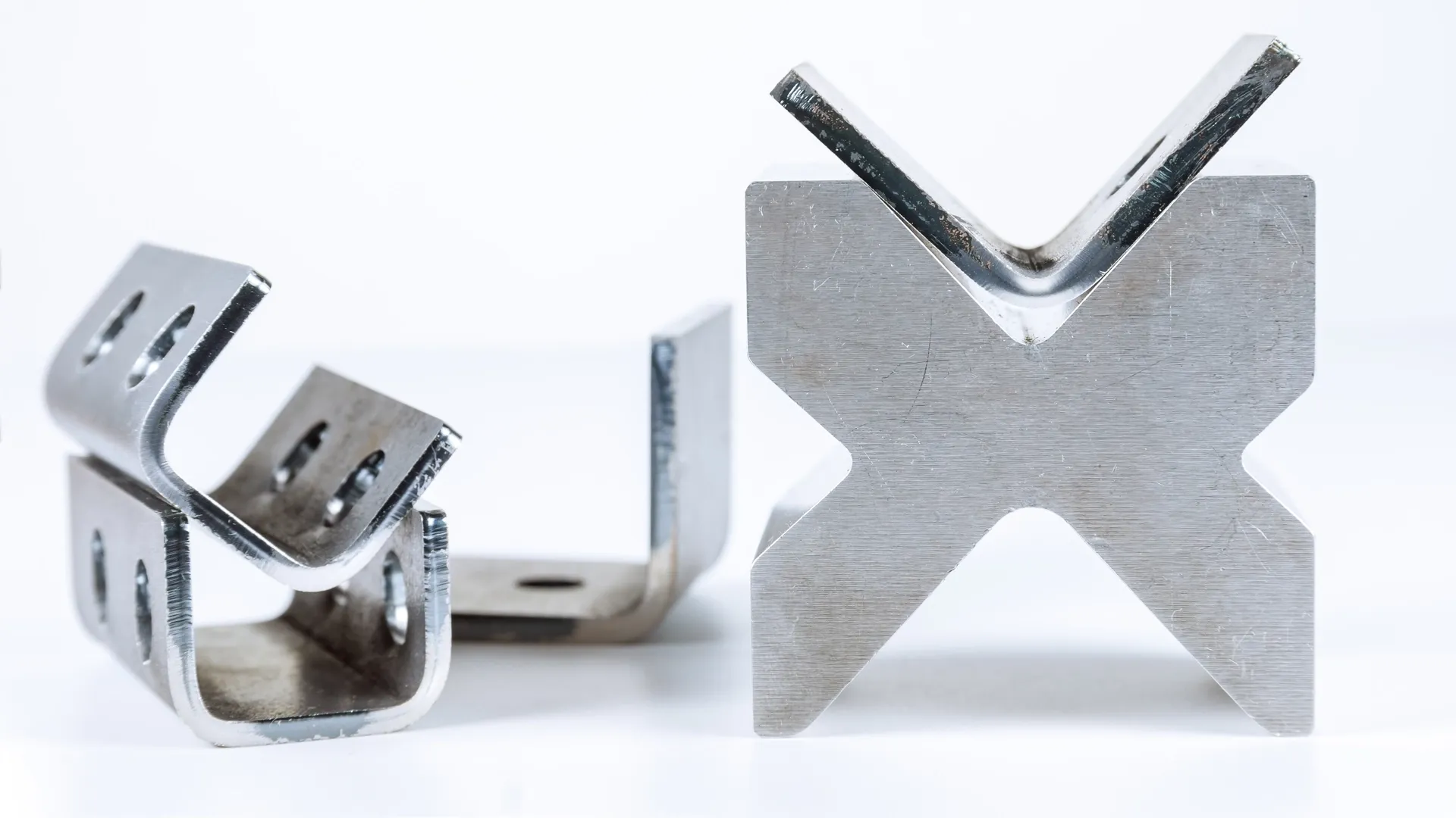 Laser-cut steel U-brackets next to an X-shaped stainless steel test coupon