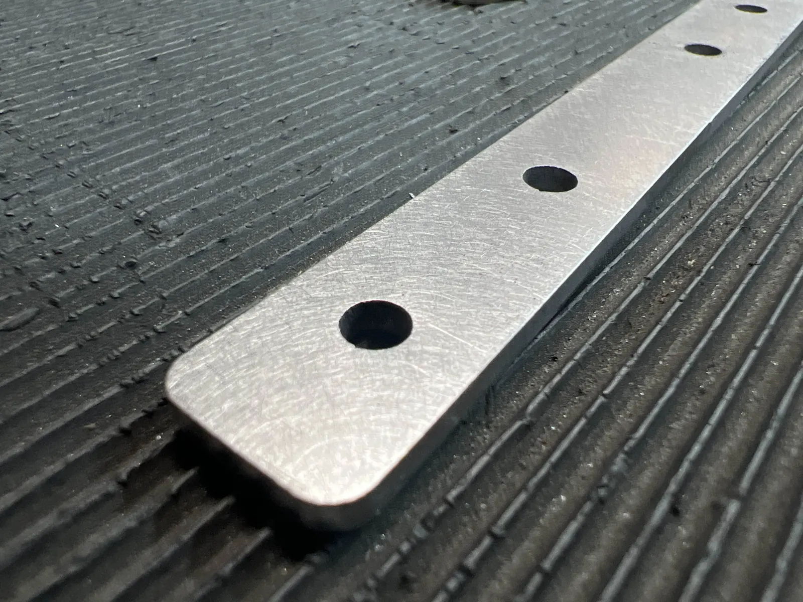 Close-up of a laser-cut aluminum strip with deburred, smoothed edges and round holes