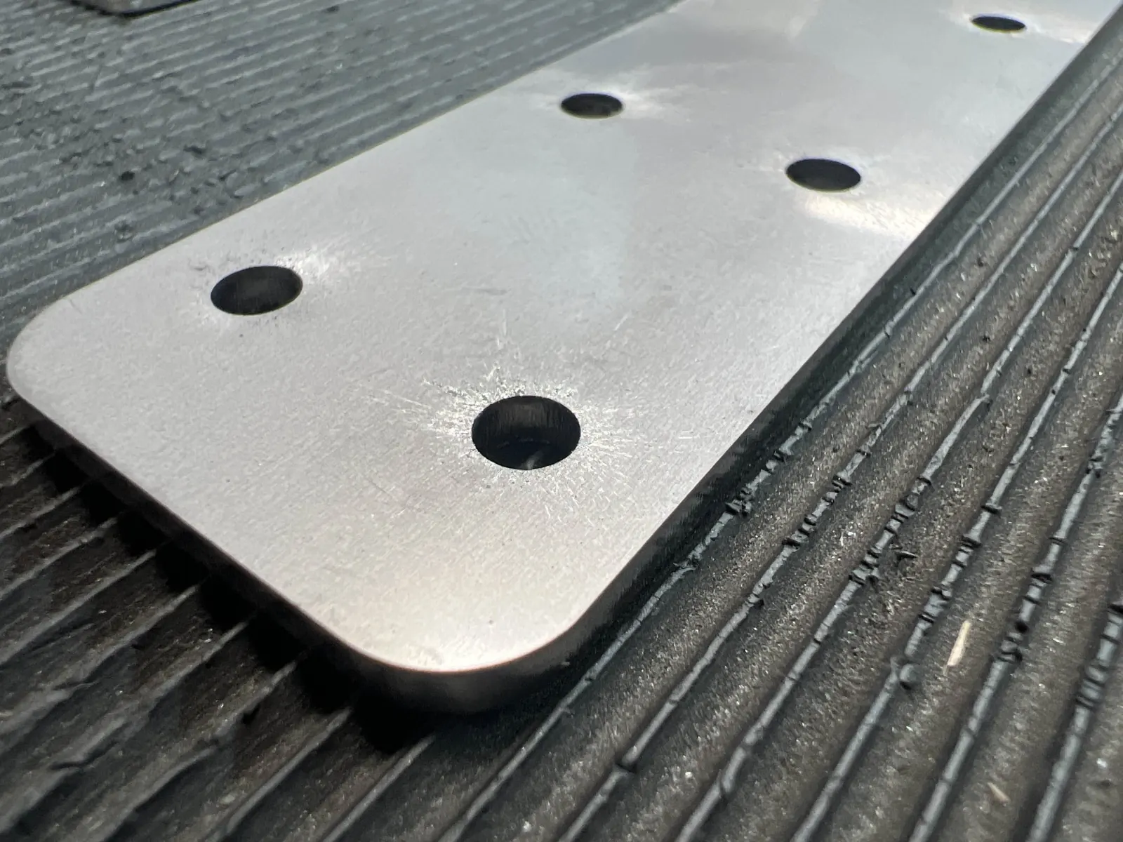 Close-up of a laser-cut aluminum strip with raw, non-deburred edges and round holes